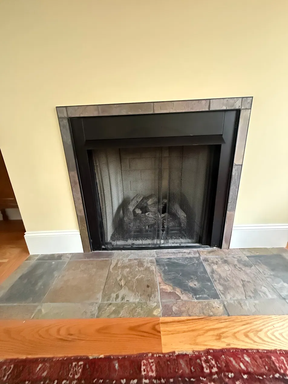 The finished fireplace surround — slim slate-tone tile replacing the old arched masonry