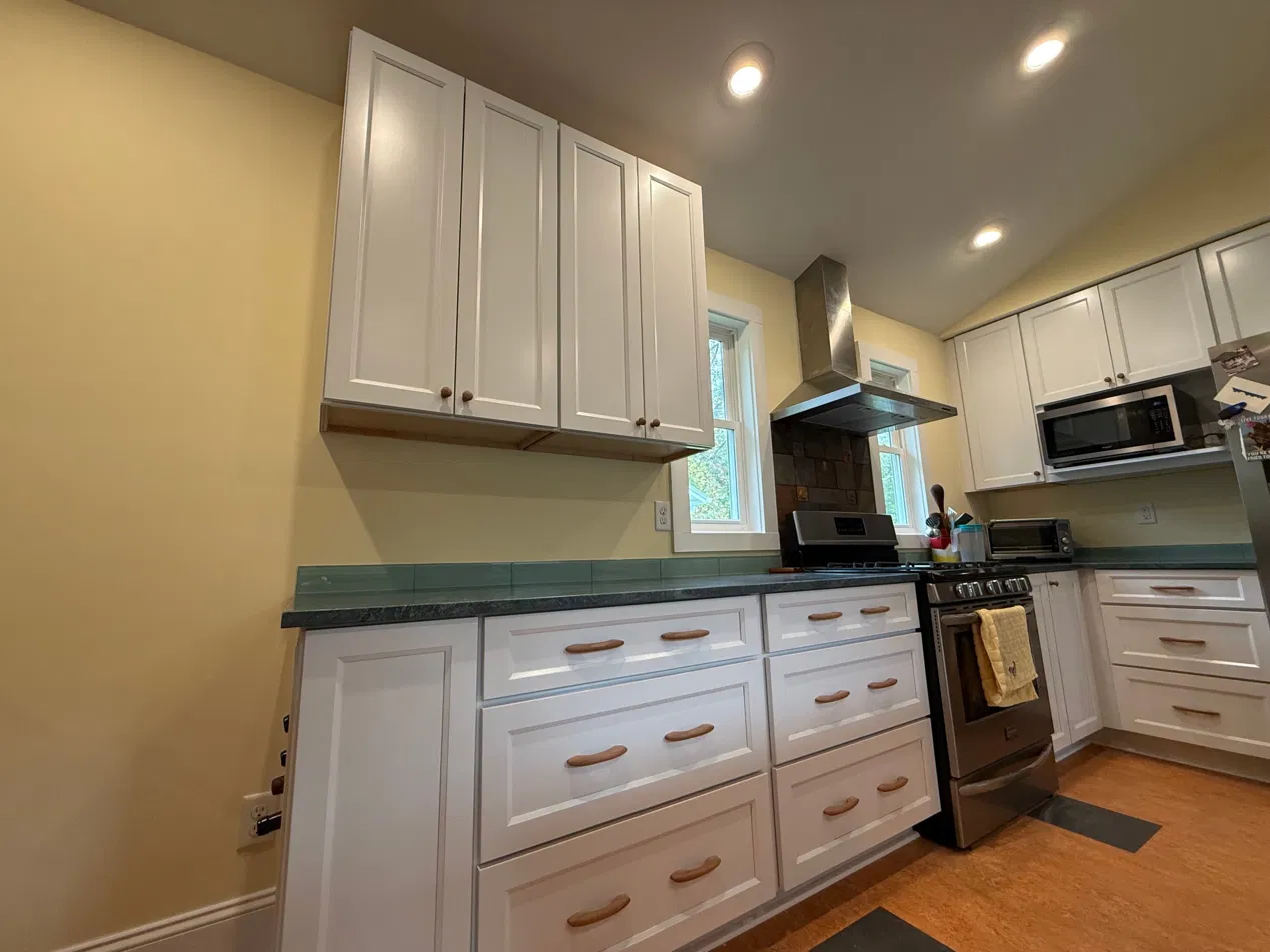 The finished kitchen — white shaker cabinetry, soapstone countertops, glass tile backsplash, and new range hood