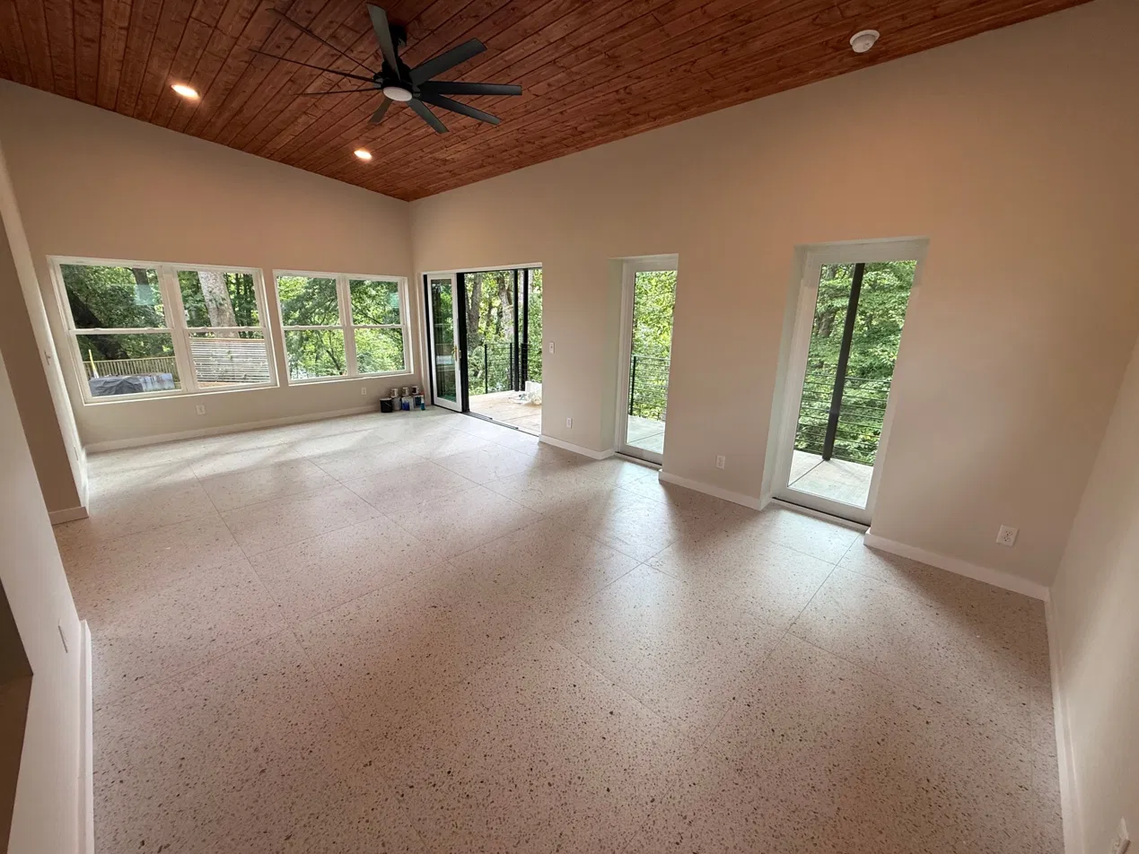The finished interior with multi-panel slider fully open — trees visible, wood ceiling, polished concrete floor