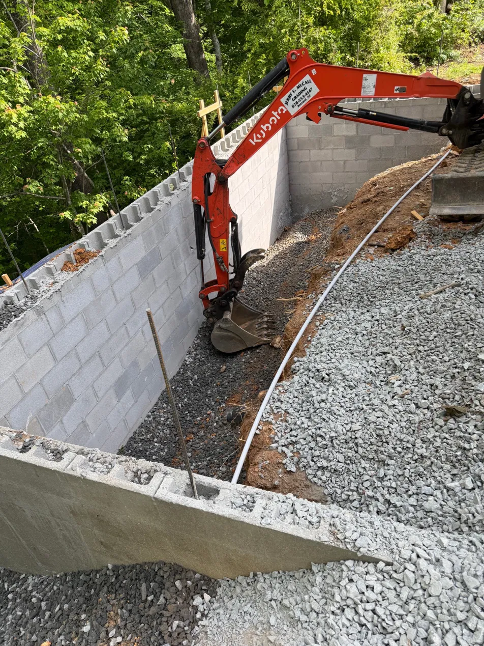 Rebuilt block foundation walls with Kubota excavator doing crushed stone backfill along the hillside