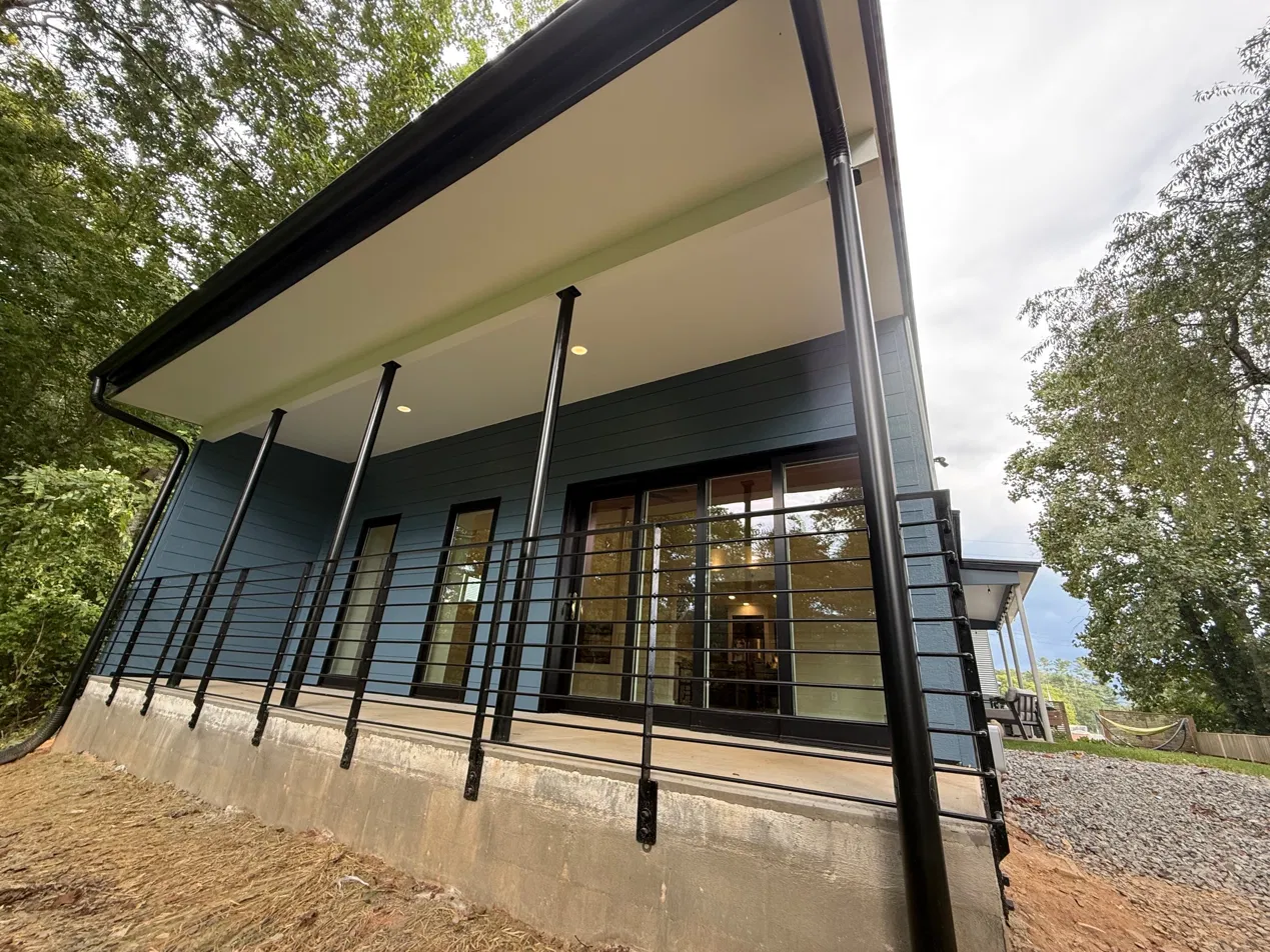 The covered porch at treetop height — black steel posts and railings, blue siding, multi-panel slider visible behind