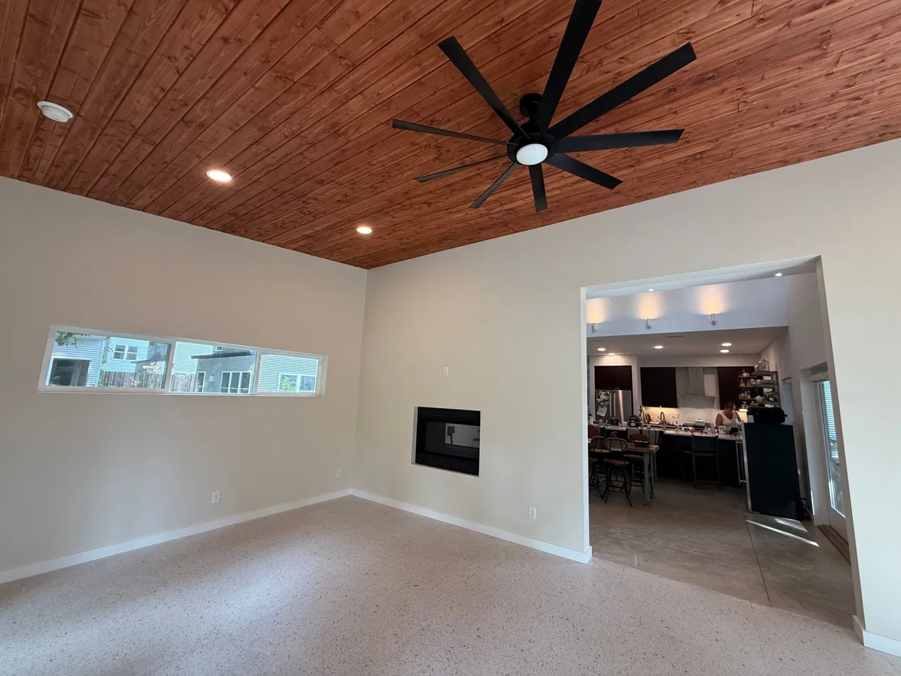 The finished interior from the kitchen side — strip window, wood vaulted ceiling, gas fireplace, opening to kitchen