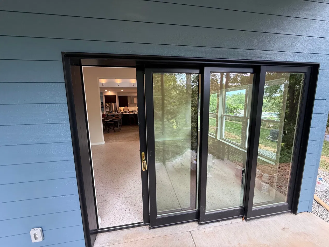 The multi-panel sliding glass door viewed from the covered porch — blue siding, four panels, kitchen visible through open panel